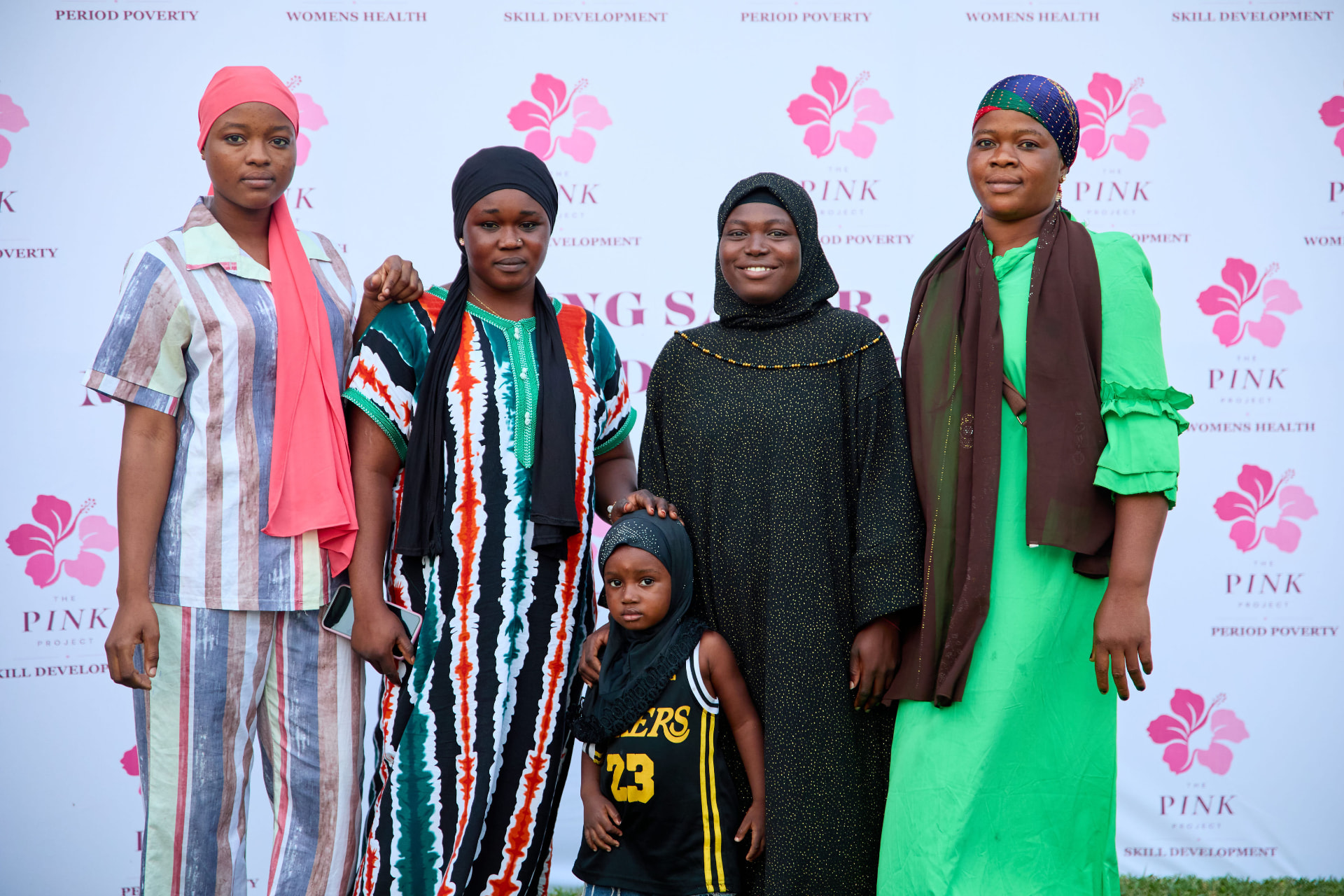 Young Kayayei women smiling together in front of The Pink Project backdrop at an outreach event
